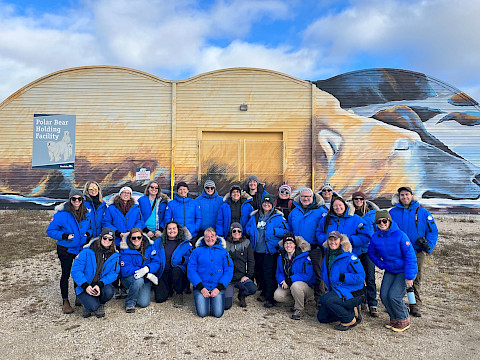 The 2023 Climate Alliance Cohort poses in front of a polar bear holding facility that is shaped like a sleeping polar bear - Shervin Hess